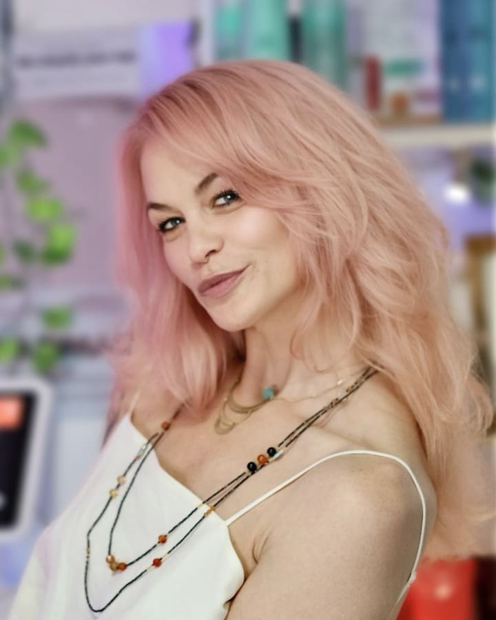 Skates, smiling, with shoulder-length pink hair and beaded necklaces.